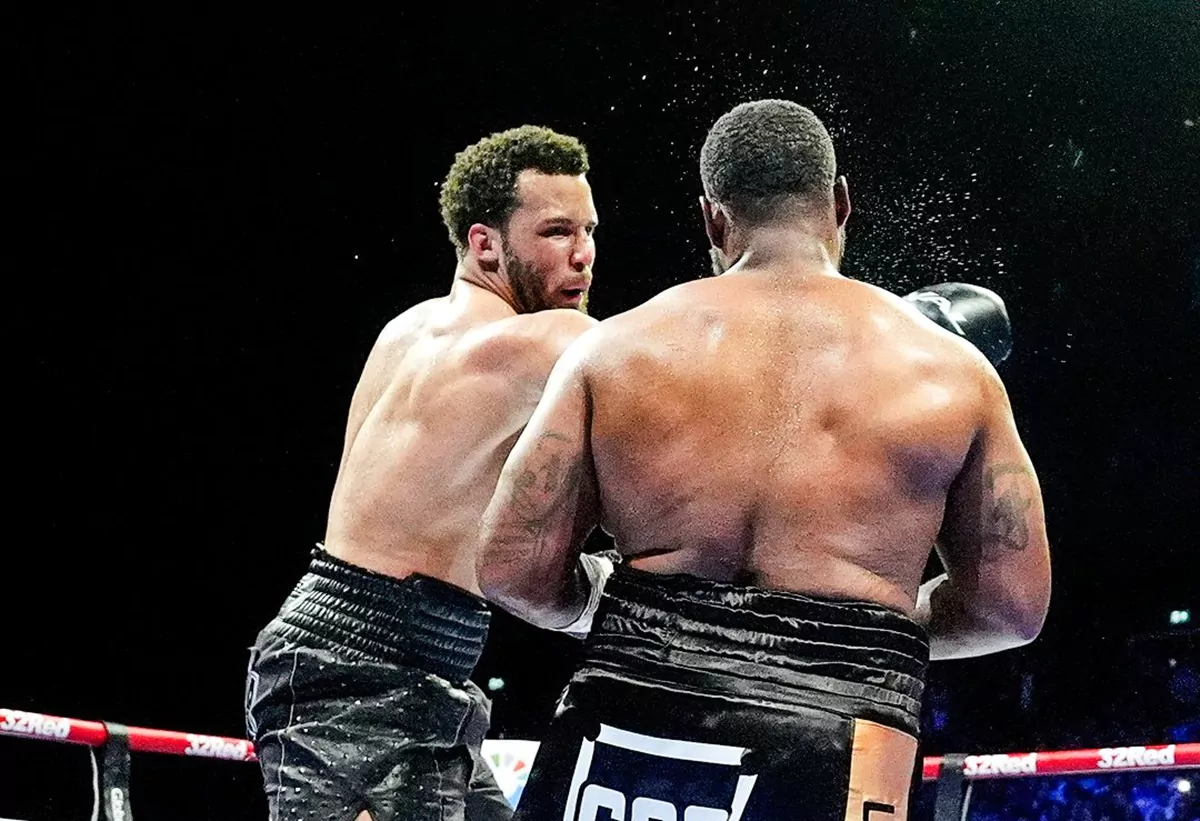 Moses Itauma (gauche, cheveux bouclés) décrochant un crochet puissant sur Jermaine Franklin (dos) dans le ring lors de leur combat de boxe poids lourds 2026, sueur projetée à l'impact — victoire aux points du prodige britannique de 20 ans